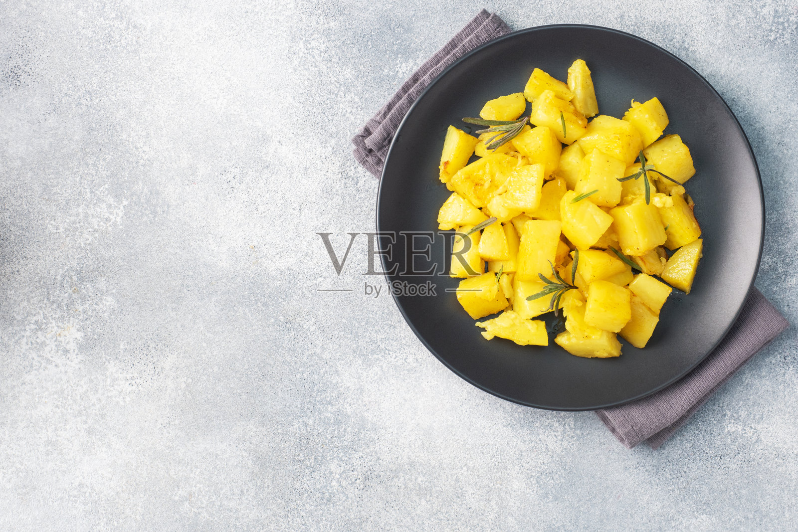 美味的烤土豆配香料、奶酪和迷迭香放在黑色陶瓷盘子上，灰色混凝土背景，复制空间。照片摄影图片