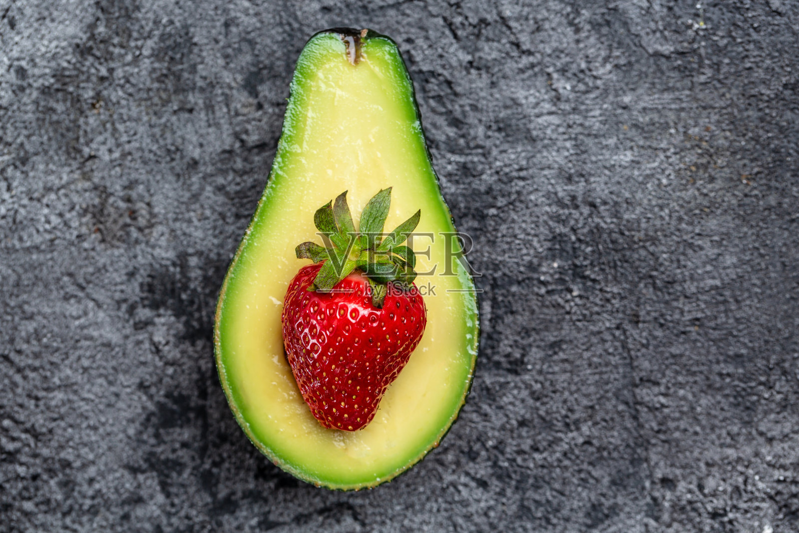 牛油果切成两半，草莓在深色的背景上。排毒的概念。长标题格式。俯视图照片摄影图片