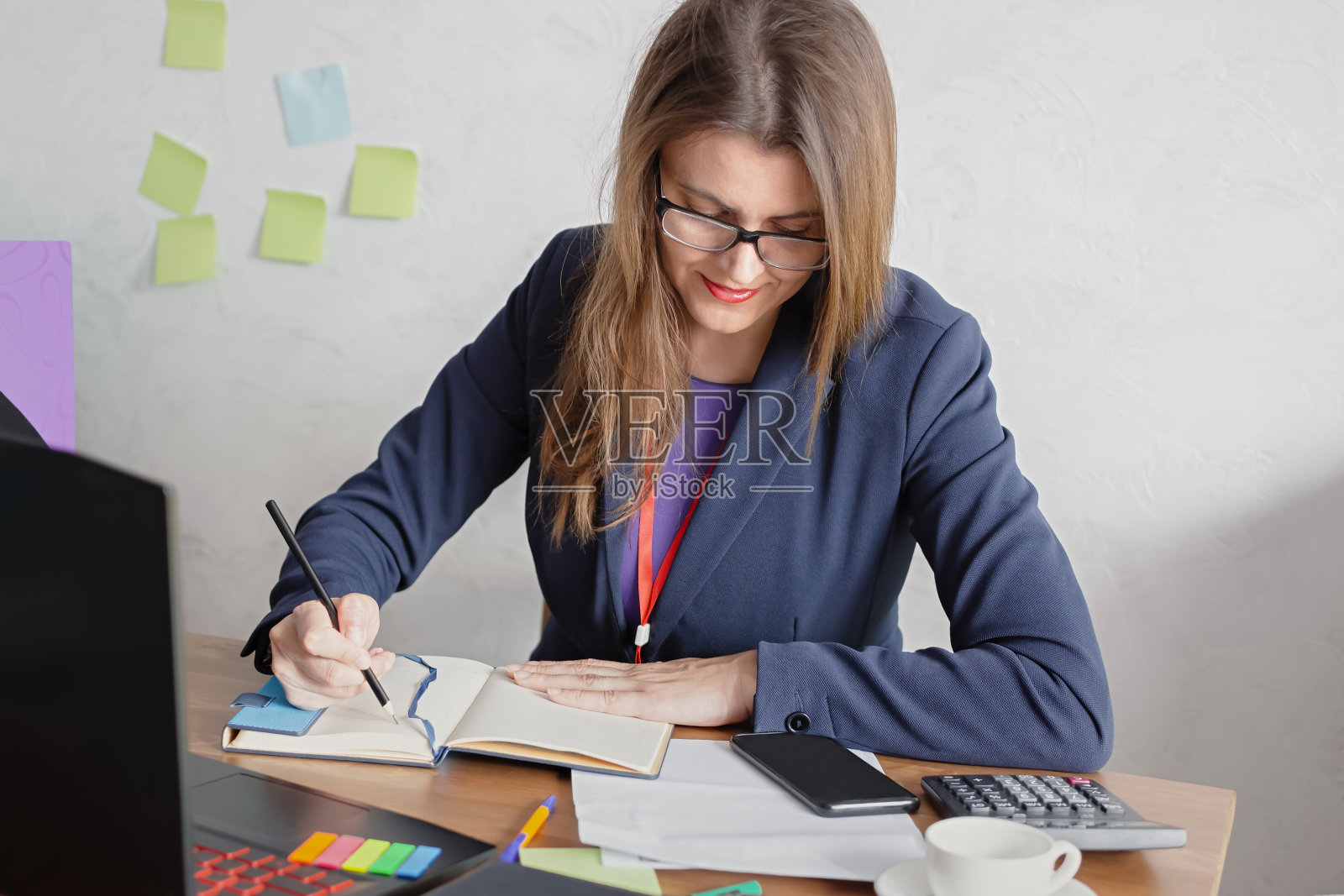 一位年轻漂亮的女商人微笑着坐在桌前，用铅笔在笔记本上写着什么照片摄影图片