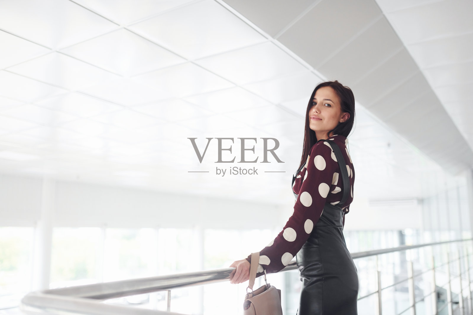 漂亮的年轻褐发女人在室内的黑色裙子在办公室或机场。有空闲时间照片摄影图片