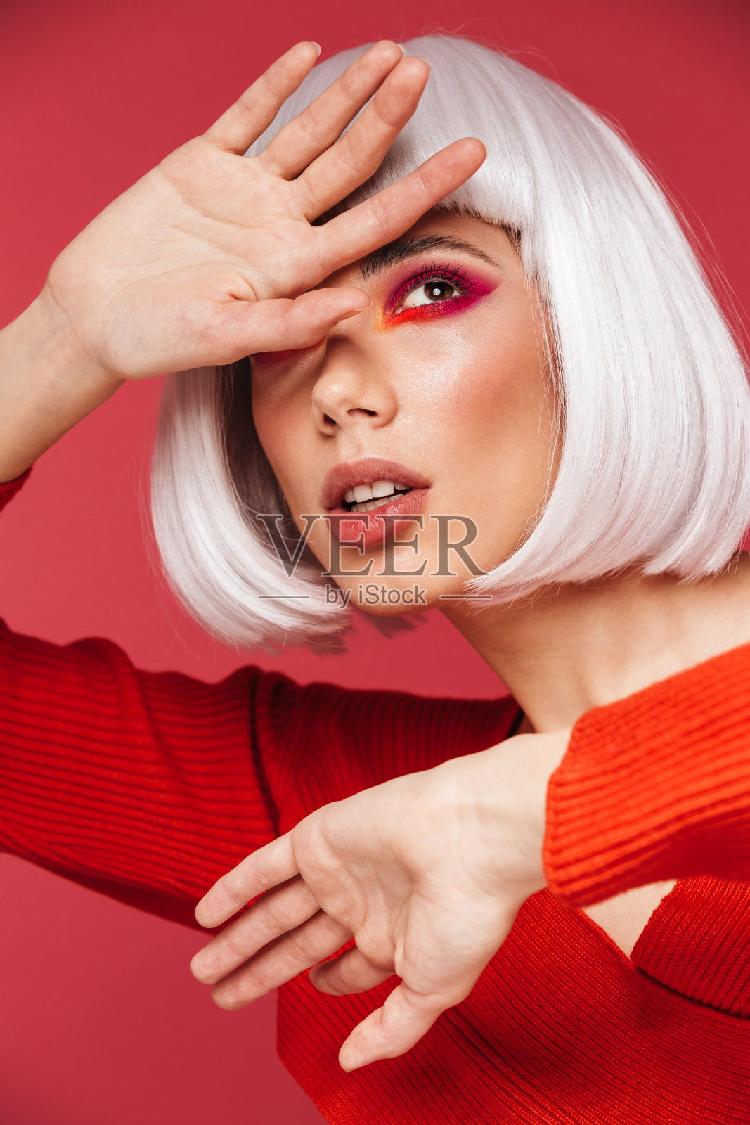 美丽的年轻女子孤立在红色的墙背景与明亮的化妆摆姿势。照片摄影图片