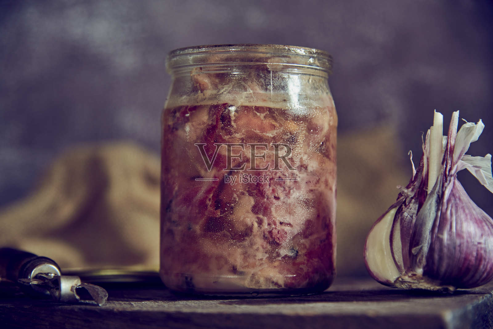 一个装着自制炖菜的玻璃罐子，还有一颗蒜头放在砧板上。照片摄影图片