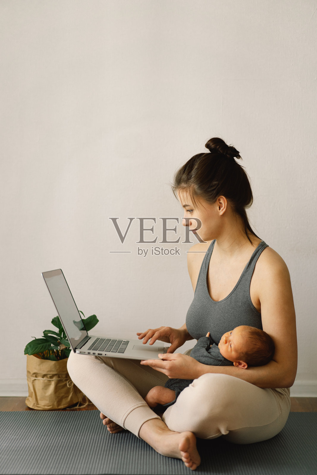 母亲抱着刚出生的儿子，在家里用电脑工作。现代母亲和自由职业。使用技术。照片摄影图片