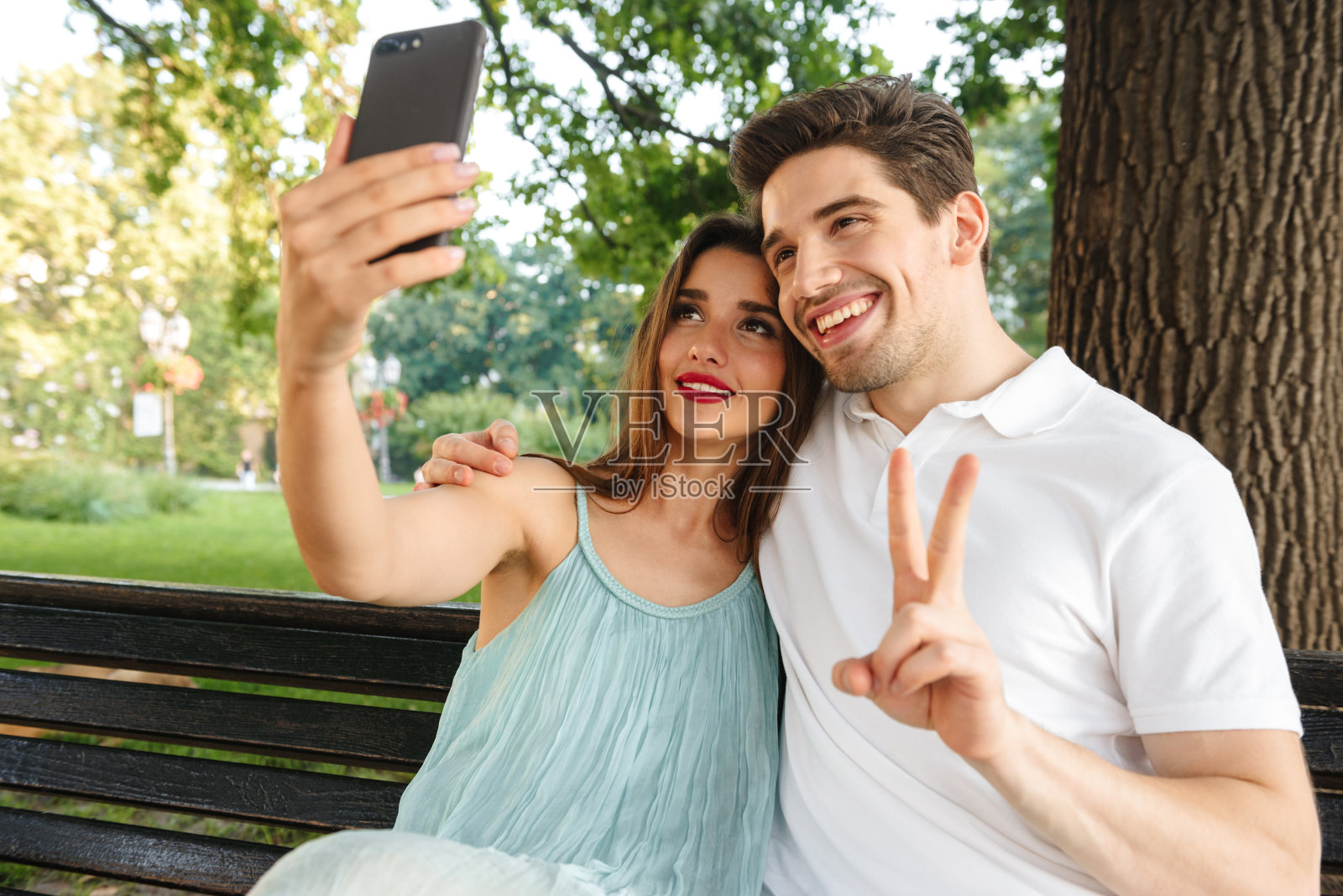 一对情侣坐在户外，用手机自拍。照片摄影图片