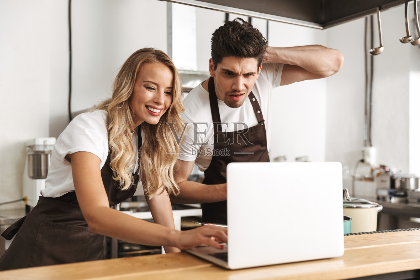 感情丰富的年轻朋友，相爱的厨师夫妇在厨房用笔记本电脑做饭。照片摄影图片