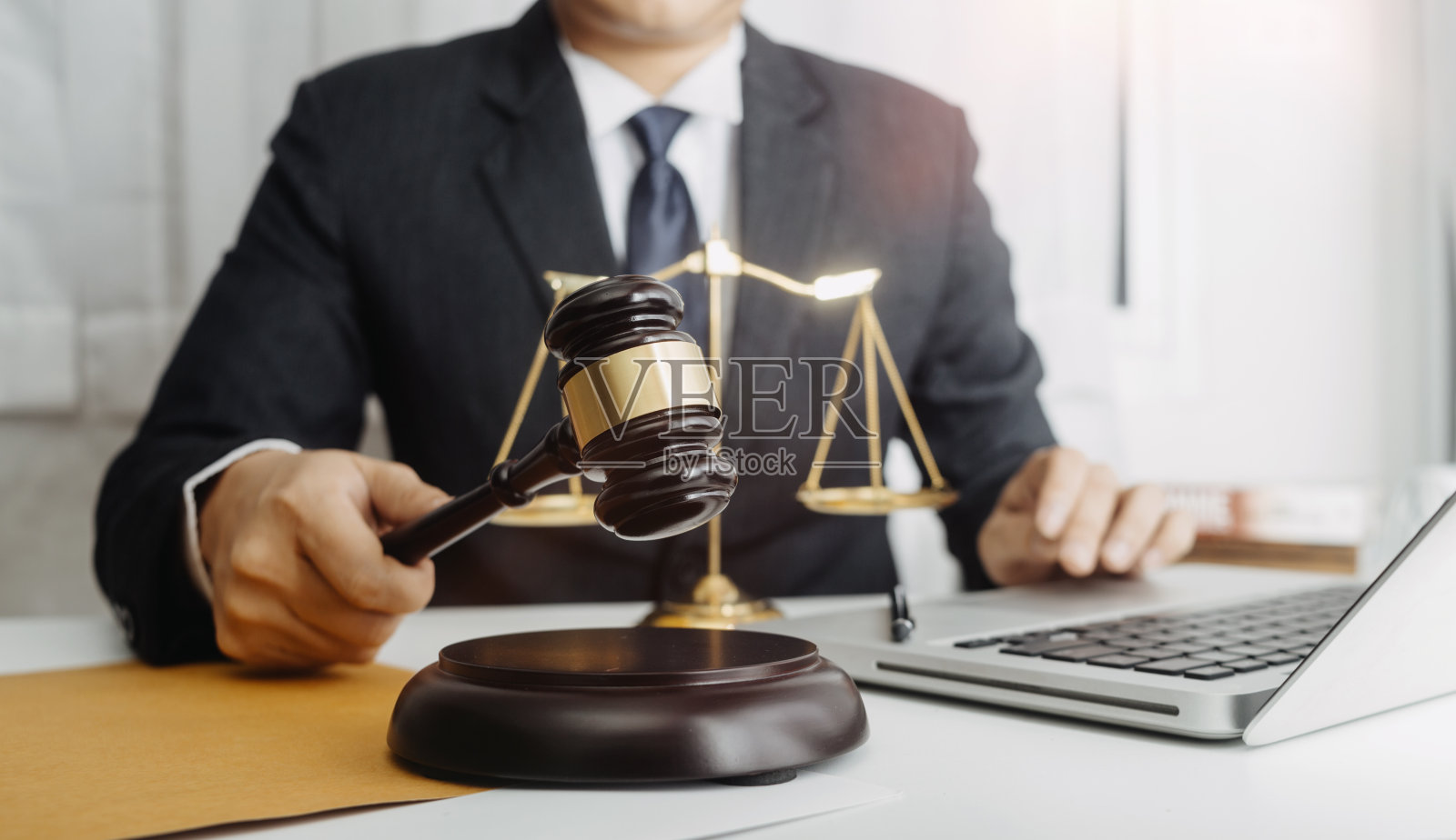 正义与法律观念。男法官在法庭上用木槌工作，电脑和对接键盘，眼镜，在晨光下放在桌子上照片摄影图片