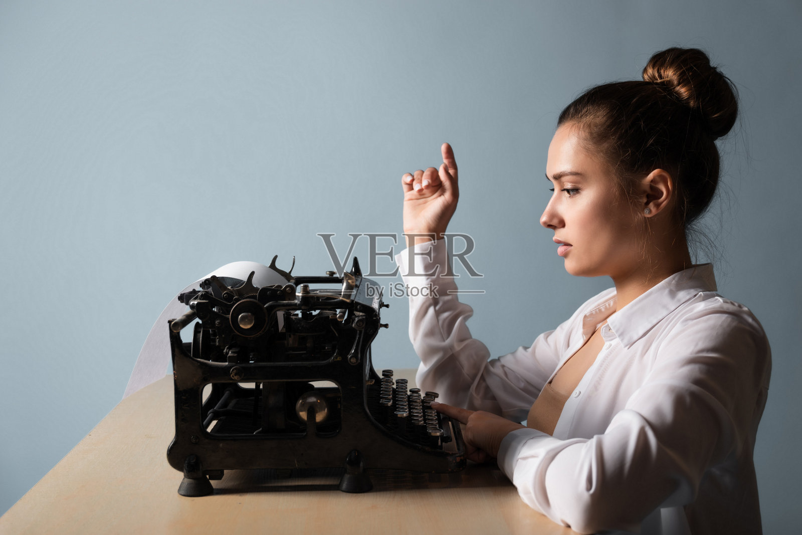 年轻女作家在打字机前写一篇文章。一位作家坐在桌子旁，手里拿着一台老式打字机照片摄影图片