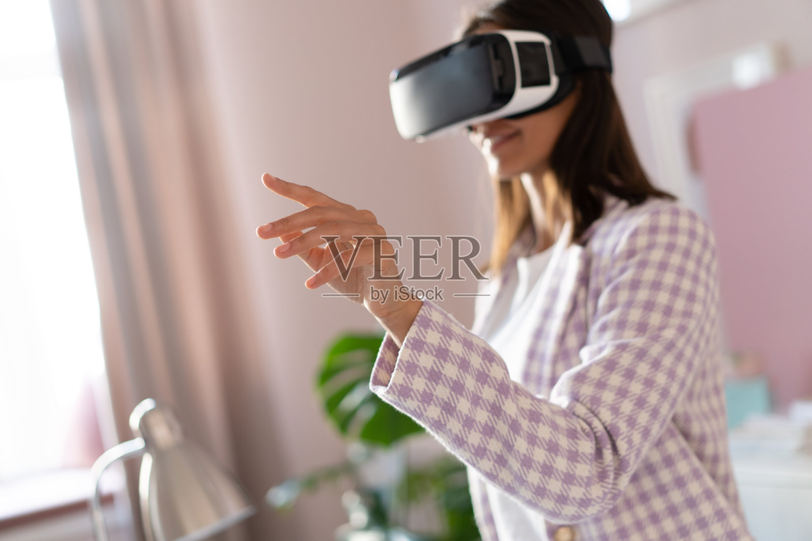 自信的年轻女子在虚拟现实头盔指向空中，而站在她的工作地点在办公室照片摄影图片