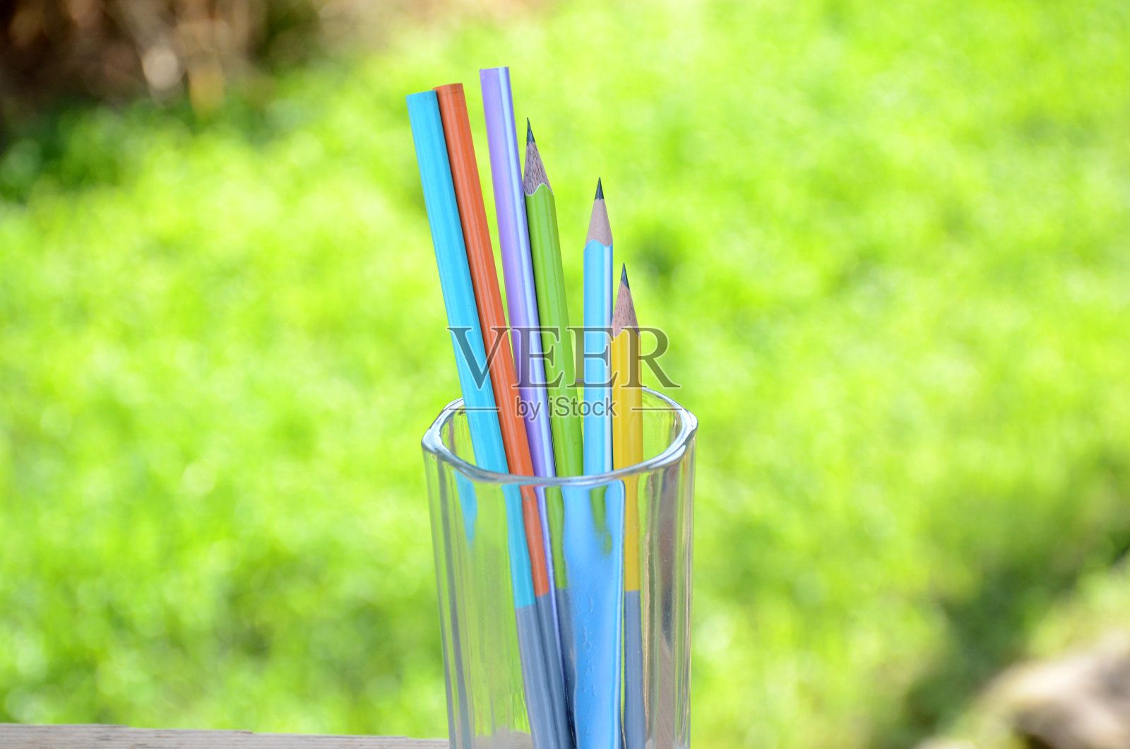 把彩色的木铅笔捆在玻璃上以绿色为背景。照片摄影图片