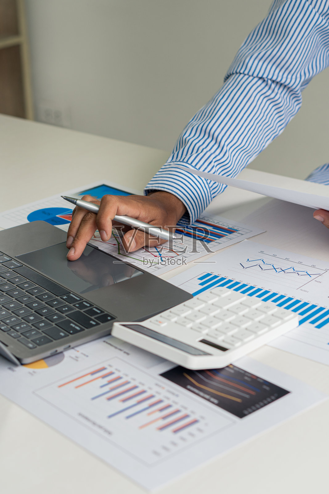 一位年轻的金融市场分析师坐在一张木桌前，用笔记本电脑在办公室里工作。商人分析文件在手图形和金融概念计算器与垂直图像。照片摄影图片