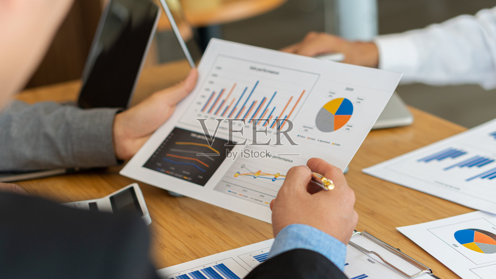 在分析金融市场时，年轻人坐在办公室的木桌子前，用笔记本电脑分析手中的文件。财务概念图表和计算器照片摄影图片