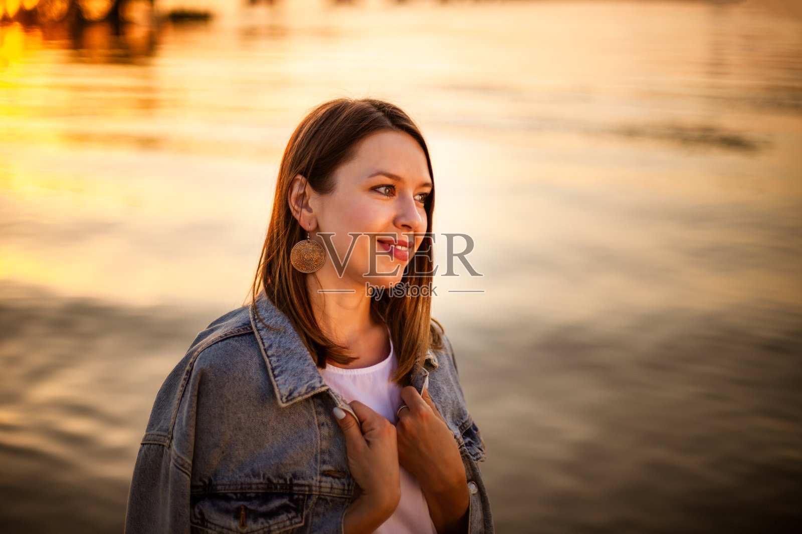 肖像在一个幸福的女人的侧面在秋天明亮的橙色日落在海边的海滩上照片摄影图片