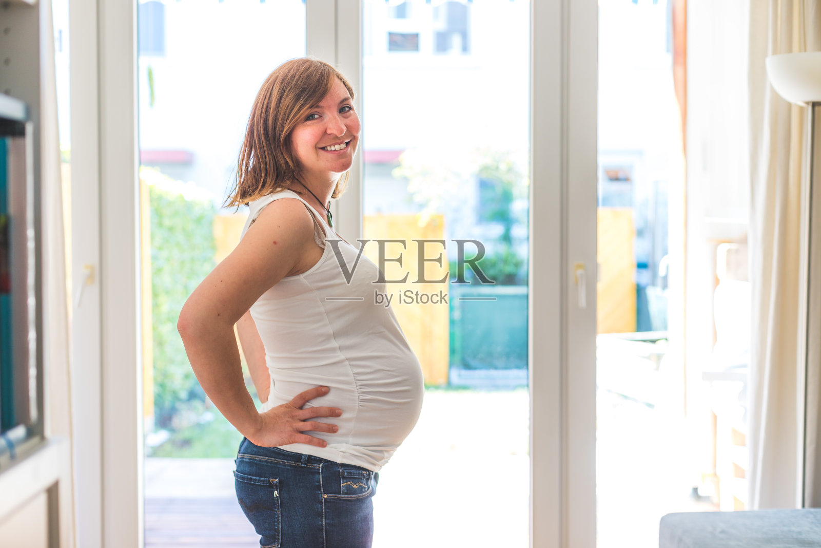 穿着蓝色牛仔裤的快乐孕妇拥抱她的肚子特写照片摄影图片