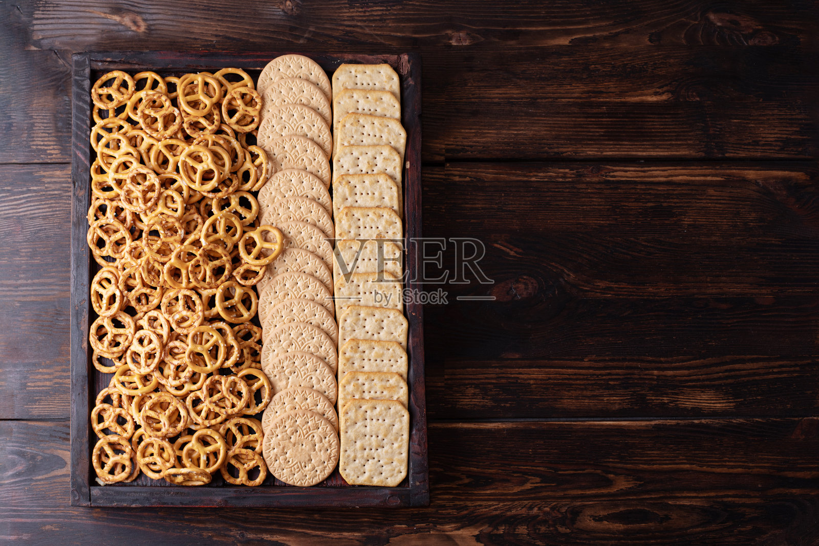 派对零食，盒子饼干，饼干和迷你盐渍椒盐卷饼在一个深色的木制背景。照片摄影图片