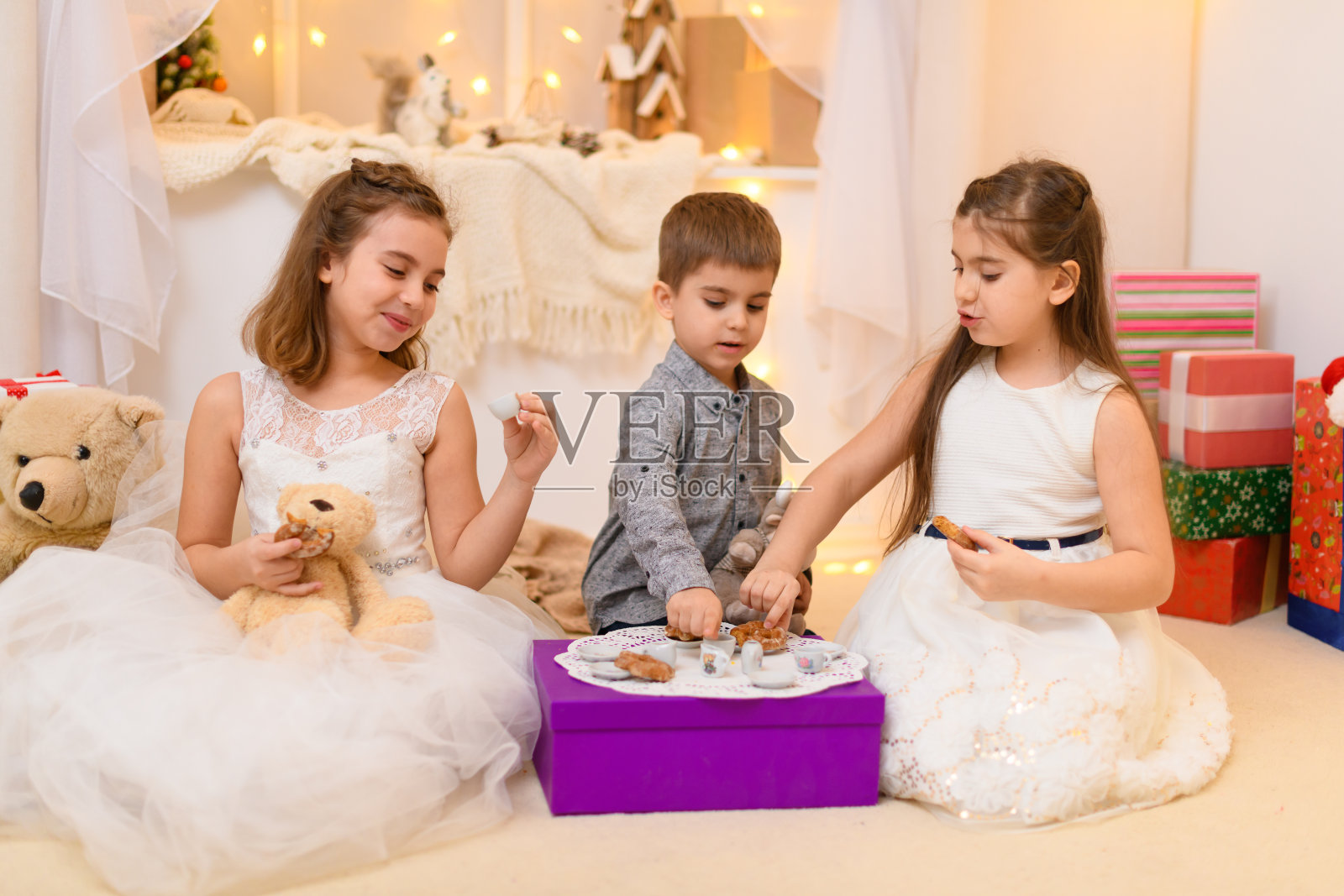 孩子们在家里喝茶，吃饼干，玩玩具盘子，里面装饰着节日灯和礼物照片摄影图片