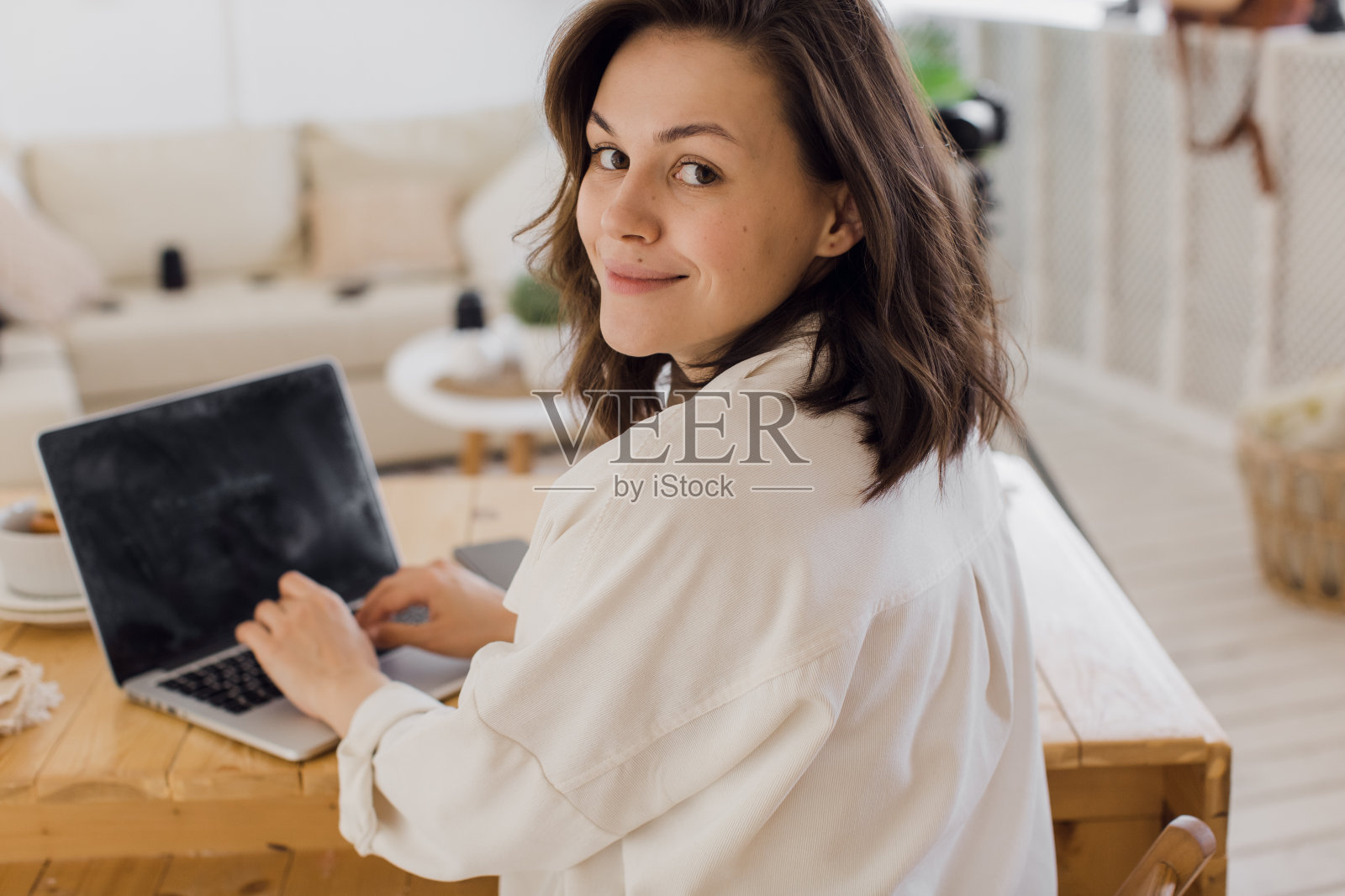 快乐年轻美丽的女人使用笔记本电脑在她的现代明亮的公寓照片摄影图片