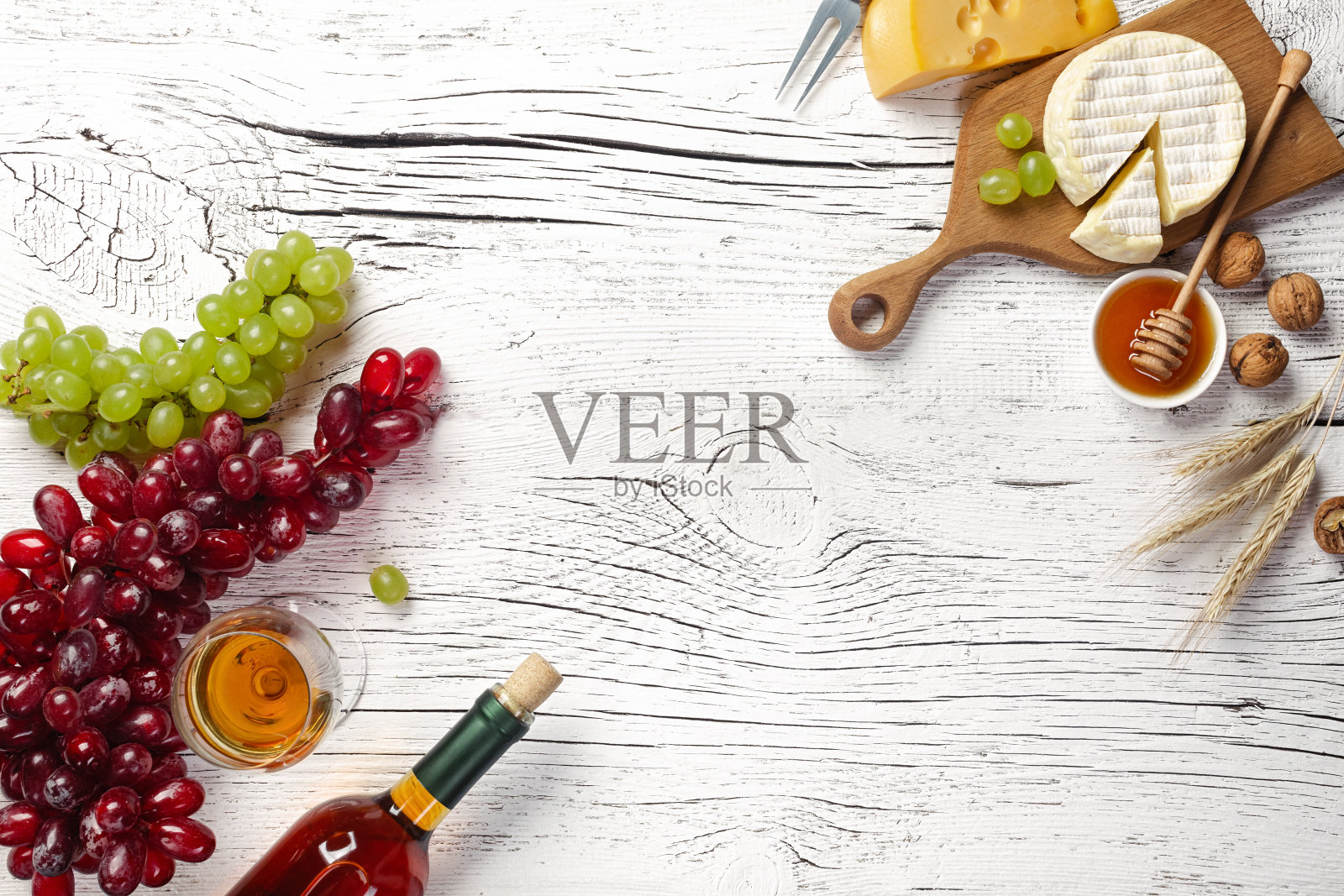 白色的酒瓶，葡萄，蜂蜜，奶酪和酒杯放在白色的木板上照片摄影图片