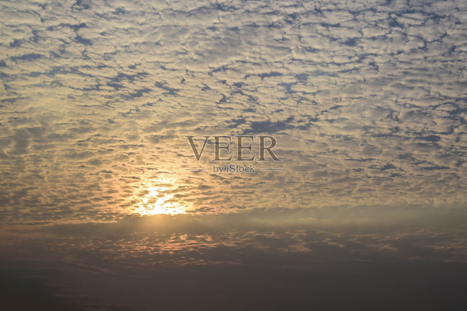 天空中有蓝色的小云朵和橙色的阳光透过天空中的云朵。照片摄影图片