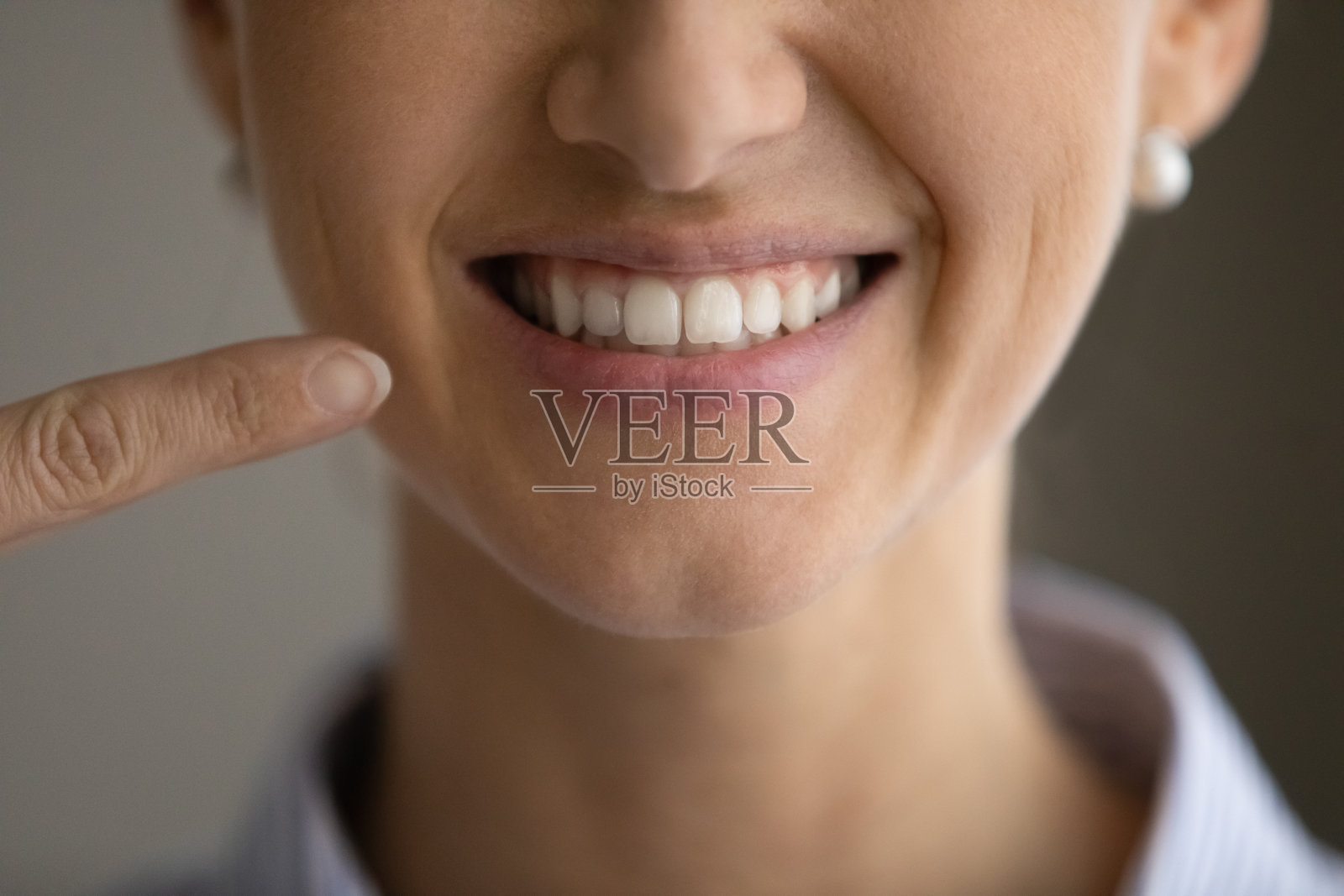 近距离快乐的年轻女子指着牙齿微笑。照片摄影图片