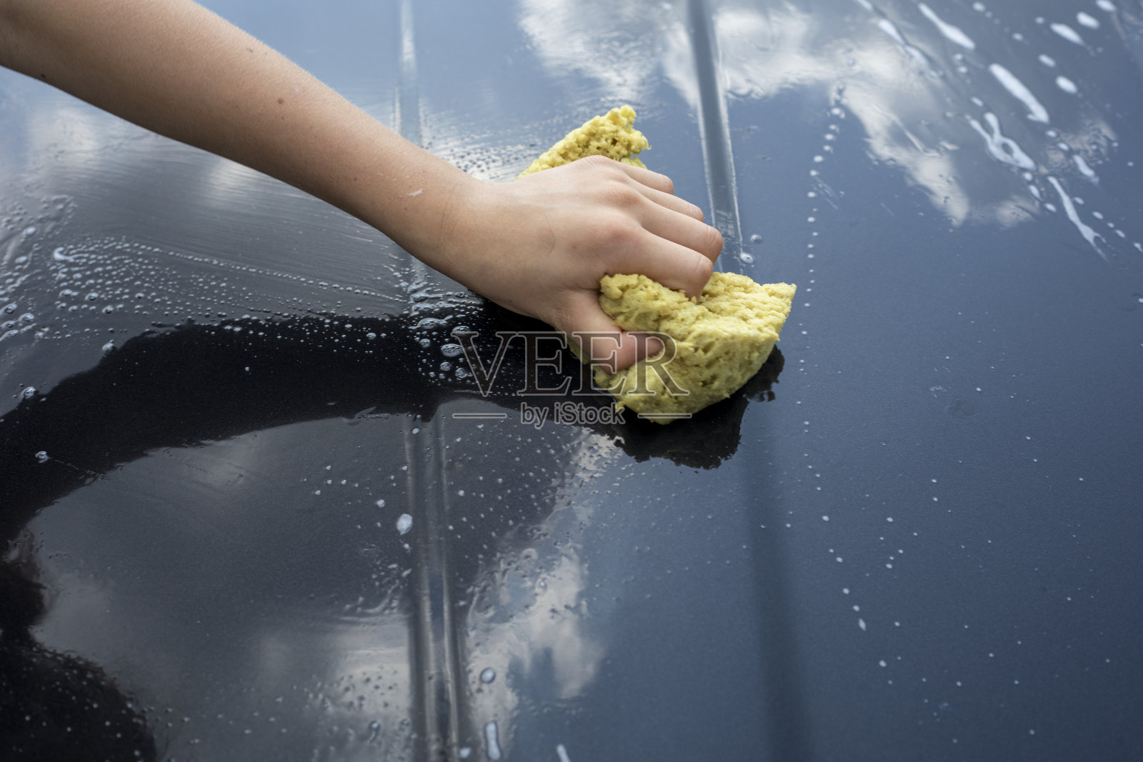 在一个阳光明媚的日子里，洪水过后在花园里清洗一辆黑色汽车的引擎盖，照片摄影图片