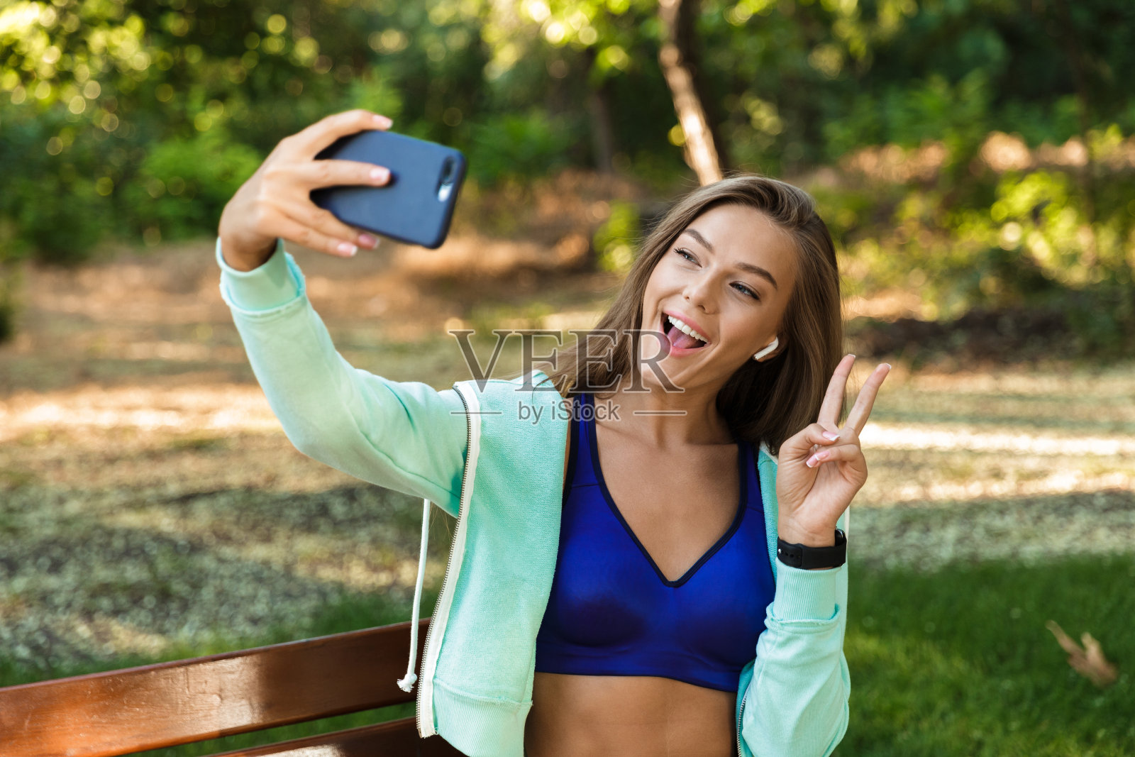 女人在公园户外用耳机听音乐用手机自拍。照片摄影图片