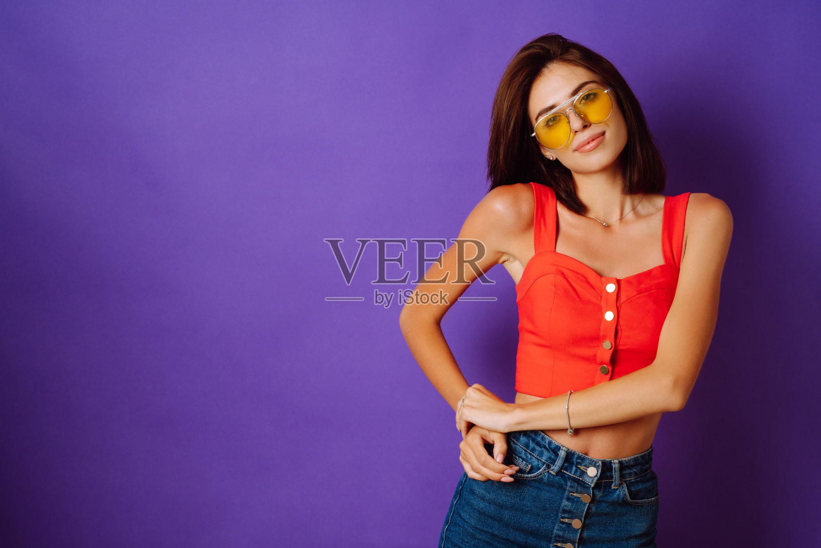 漂亮的年轻女子在红色的上衣，裙子和黄色眼镜在紫色的背景摆姿势。照片摄影图片