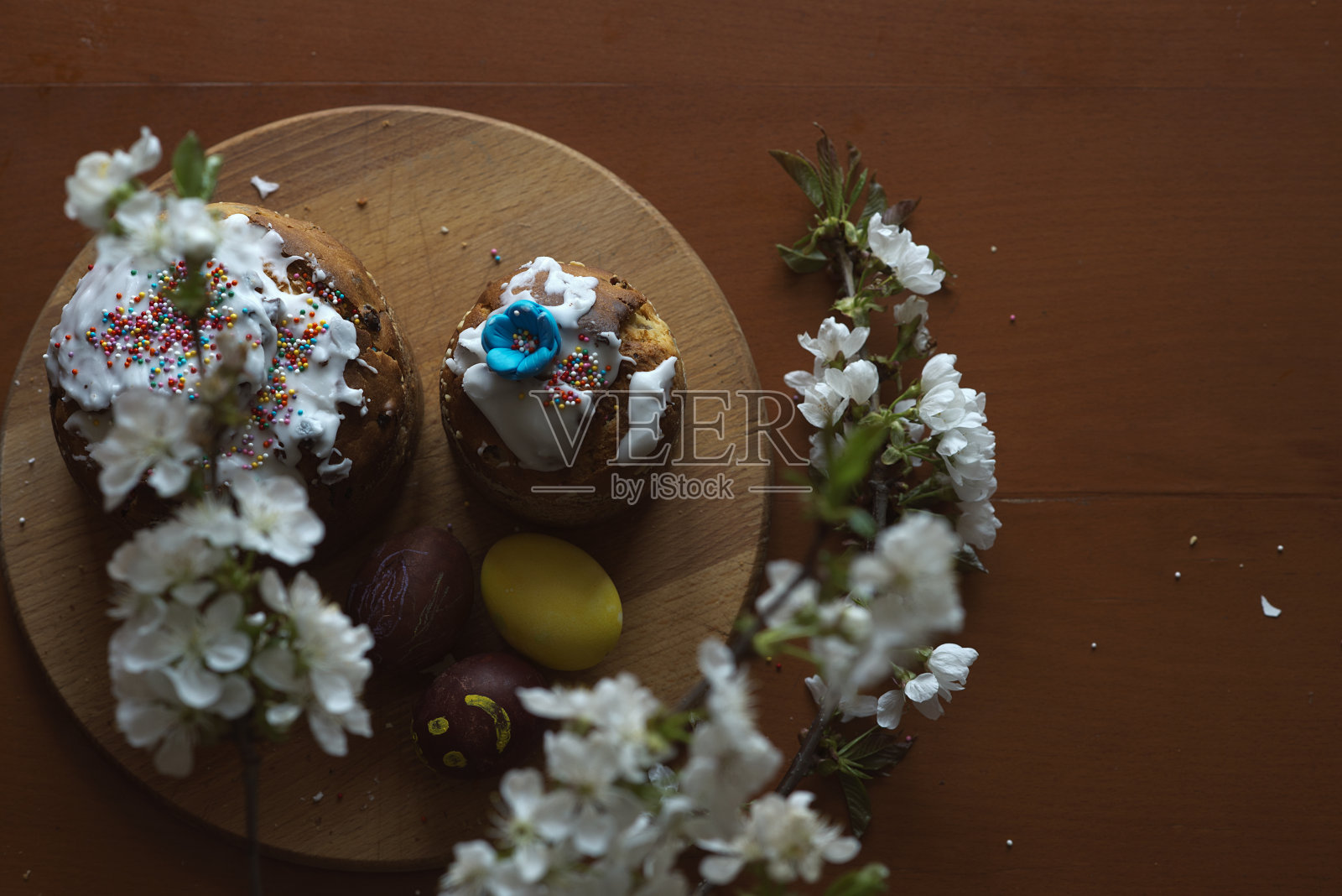 复活节、节日和传统概念。彩色彩蛋，复活节蛋糕和樱花在木制的圆形砧板上。照片摄影图片