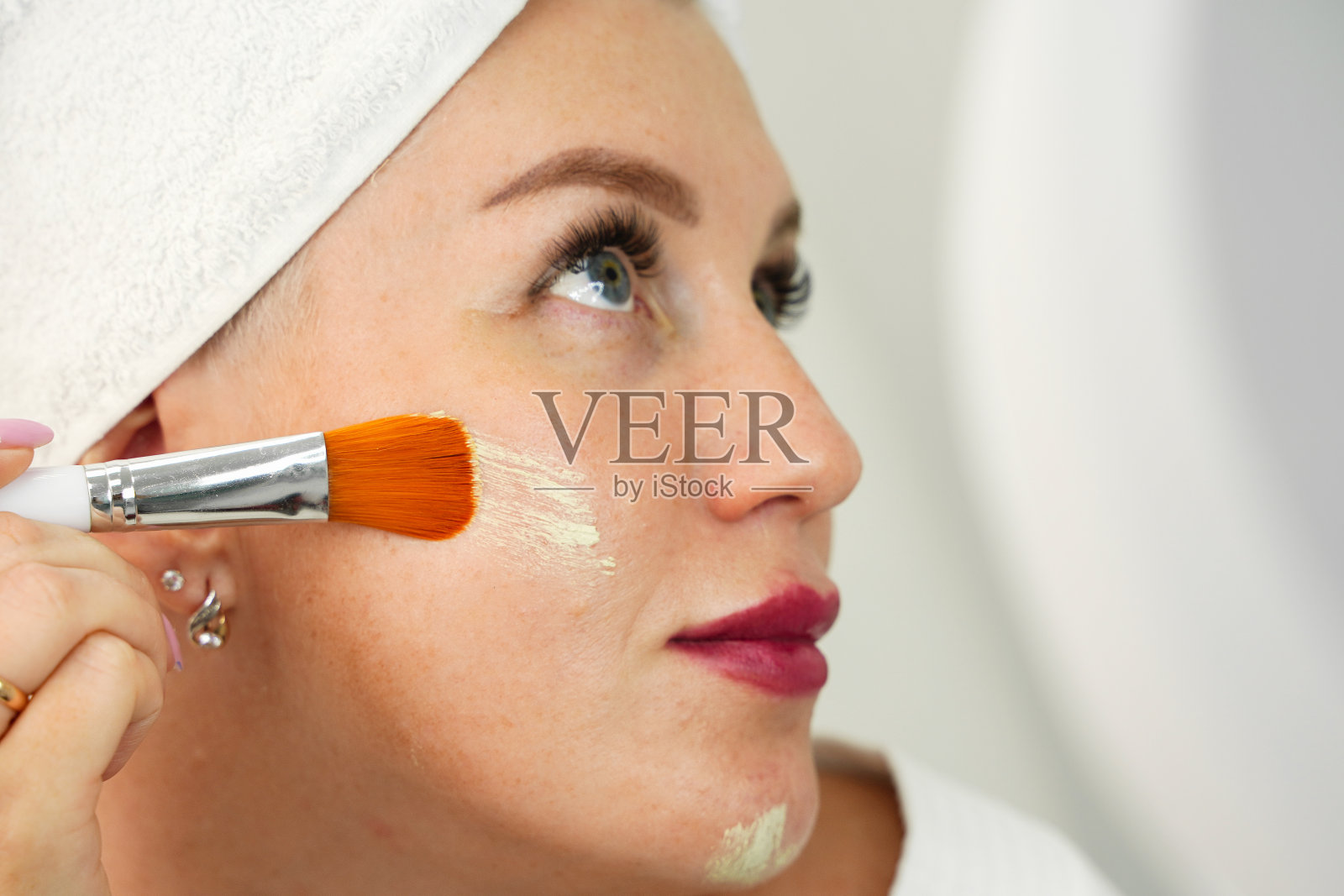 女人把化妆品涂在脸上，选择性地聚焦在皮肤上。用刷子将粉底涂在色素沉着的皮肤上。与化妆品重叠的皮肤瑕疵。照片摄影图片