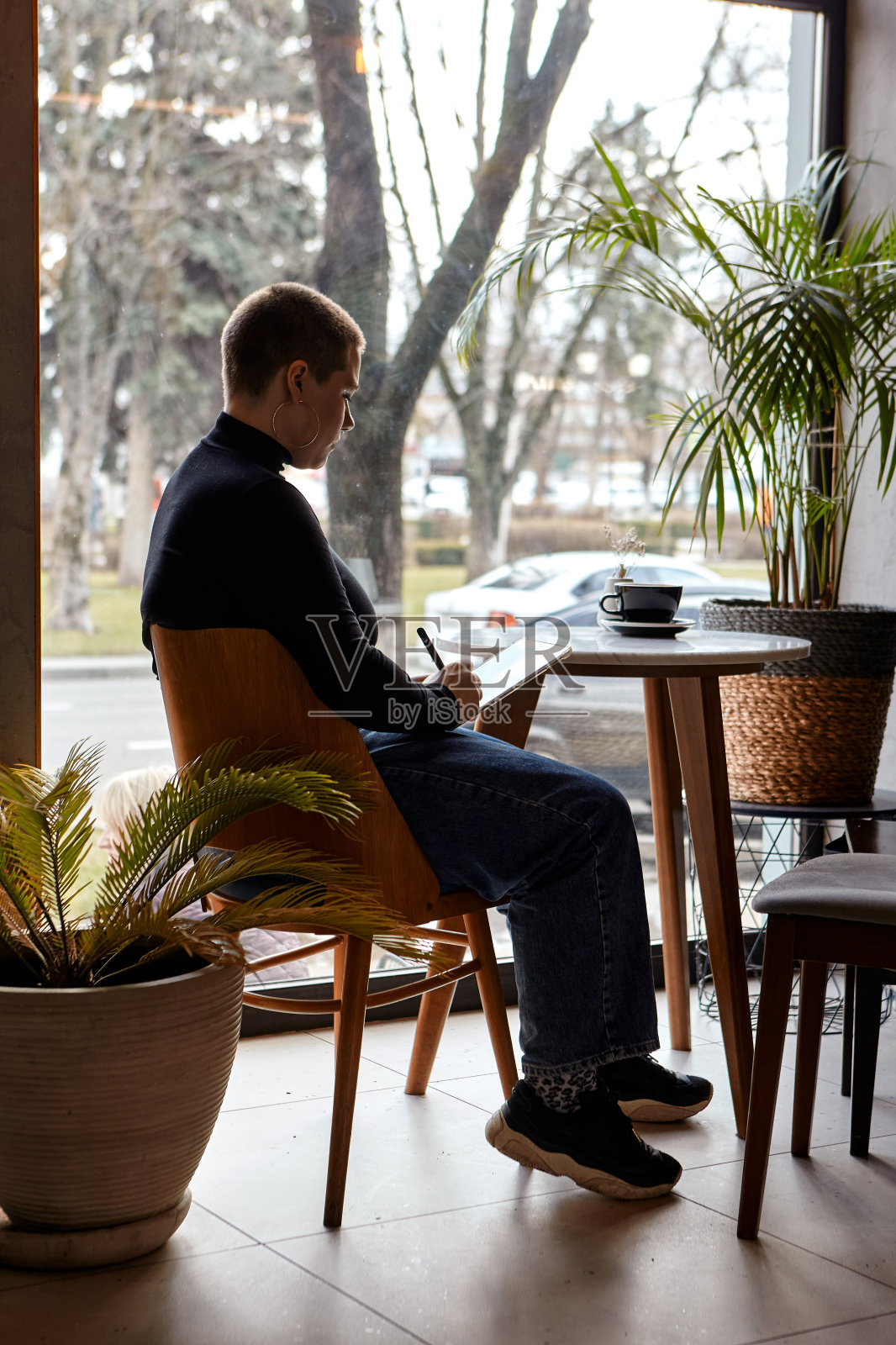 一个留着短发、穿鼻环的年轻女孩坐在咖啡馆里，在平板电脑前工作。自由职业和远程工作的概念。照片摄影图片