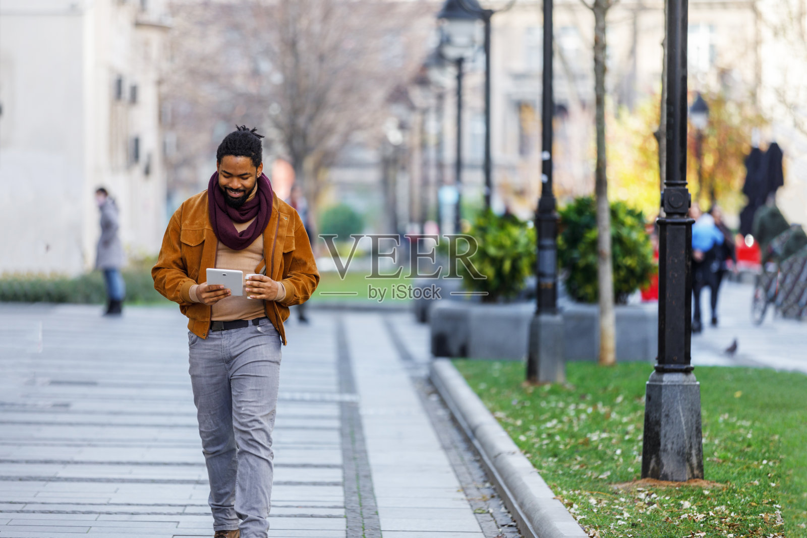 一位年轻的非洲裔美国人拿着平板电脑，一边喝咖啡，一边在市区里散步。照片摄影图片