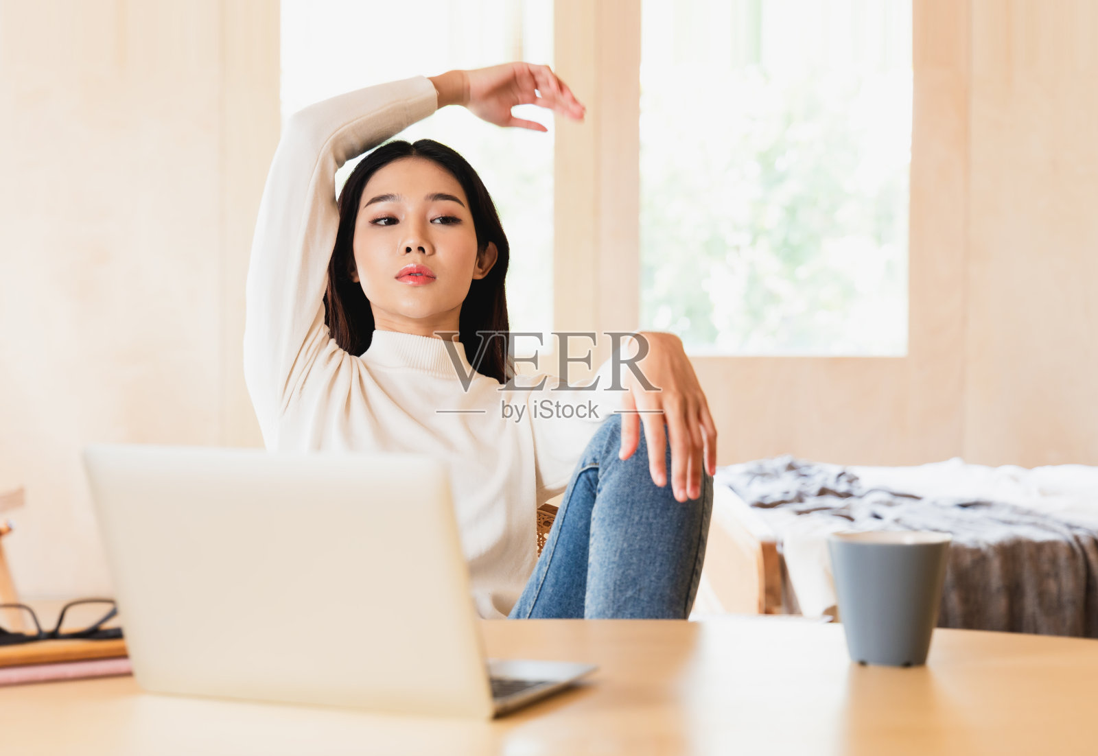 年轻的亚洲女人的肖像摆出时髦的样子。一个微笑的黑发女人自然化妆穿着时装。美丽的女模特用笔记本电脑查看在线内容和在家工作。照片摄影图片