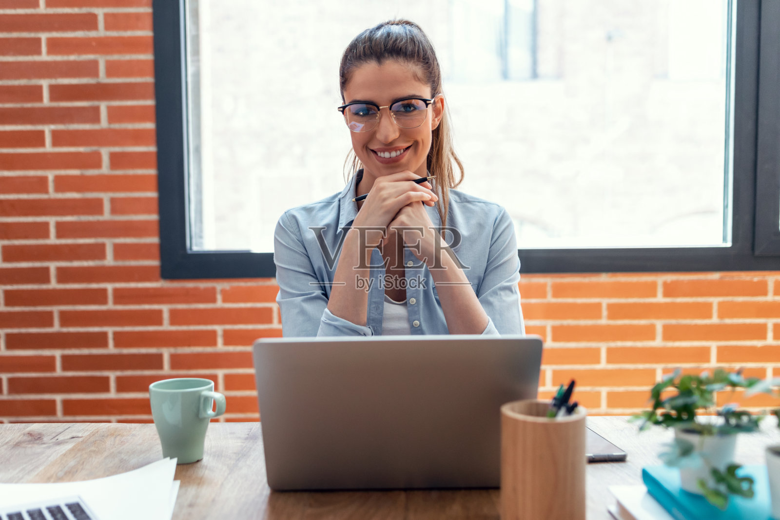 专注的年轻商业女性工作笔记本电脑，同时看着摄像头在家里的客厅。照片摄影图片