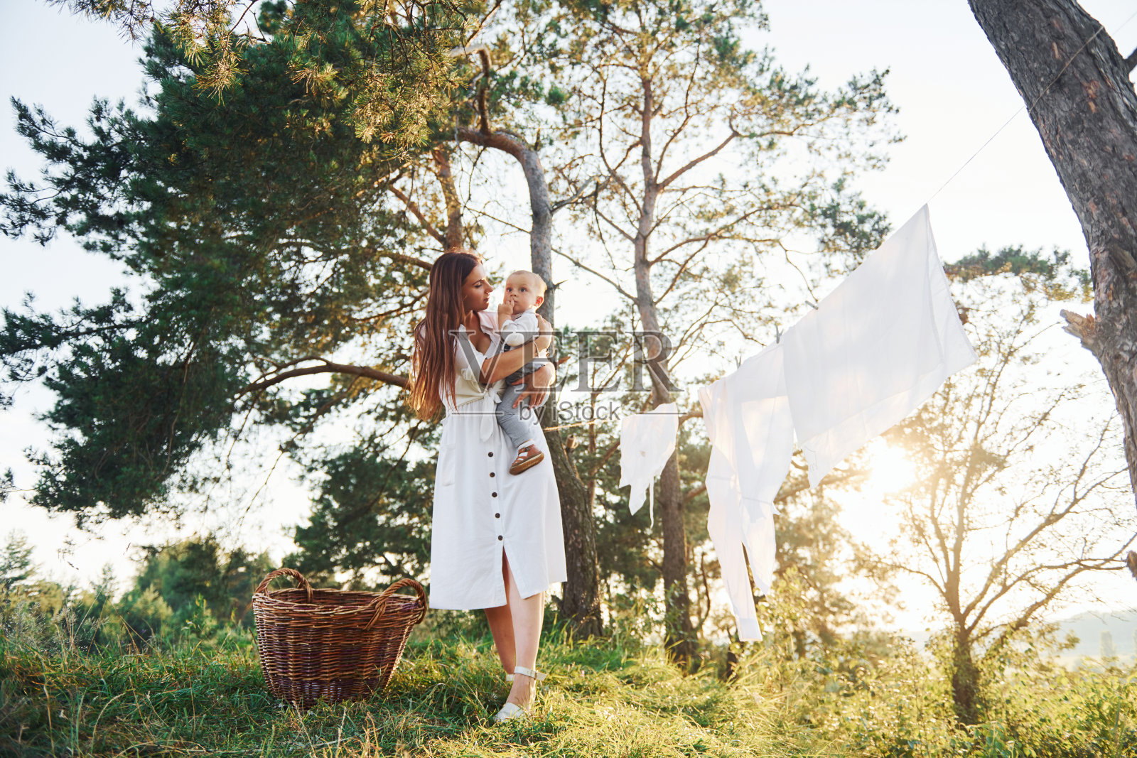干净的衣服挂在绳子上晾干。一位年轻的母亲带着她的小儿子在森林的外面。美丽的阳光照片摄影图片