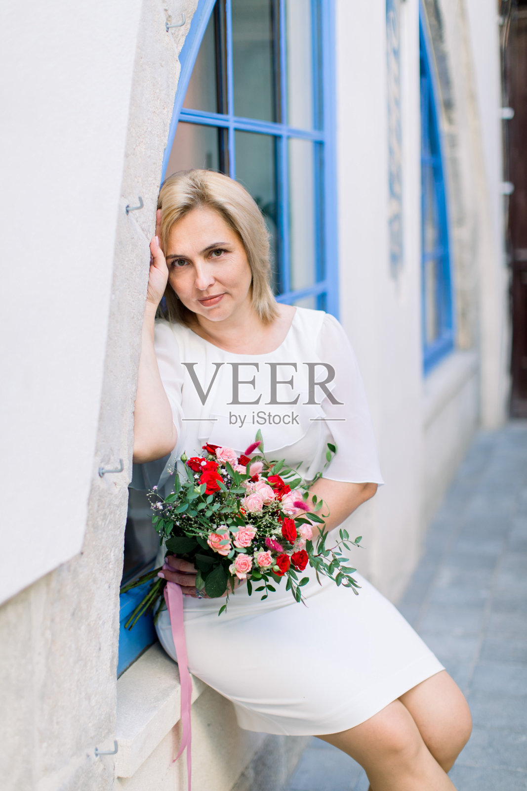 时尚的成熟女性穿着白色优雅的裙子，手持花束在城市的户外摆姿势照片摄影图片