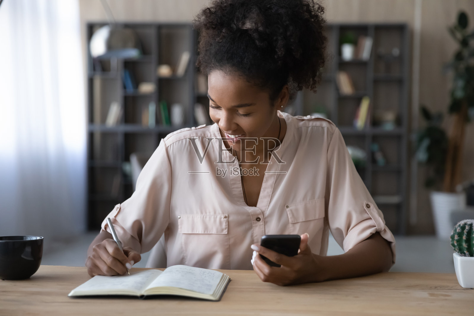 微笑的非裔美国妇女拿着电话，在笔记本上记笔记照片摄影图片