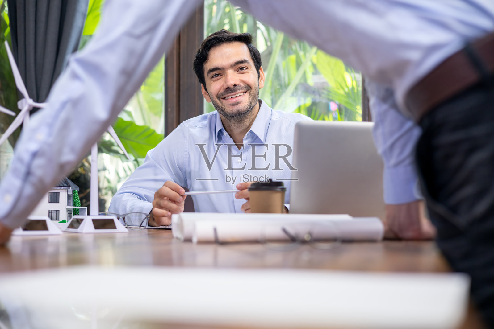 在办公室举行的风力发电机能源管理会议上，一名白人建筑师与同事们笑了起来。照片摄影图片