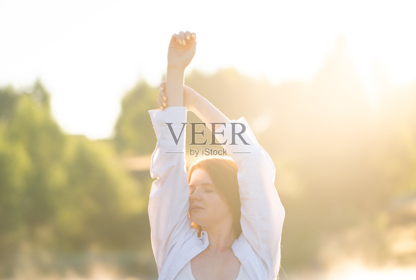 一个美丽的红发女孩穿着白衬衫在大自然中遇见了夏日的黎明。幸福和精神自由的概念。照片摄影图片