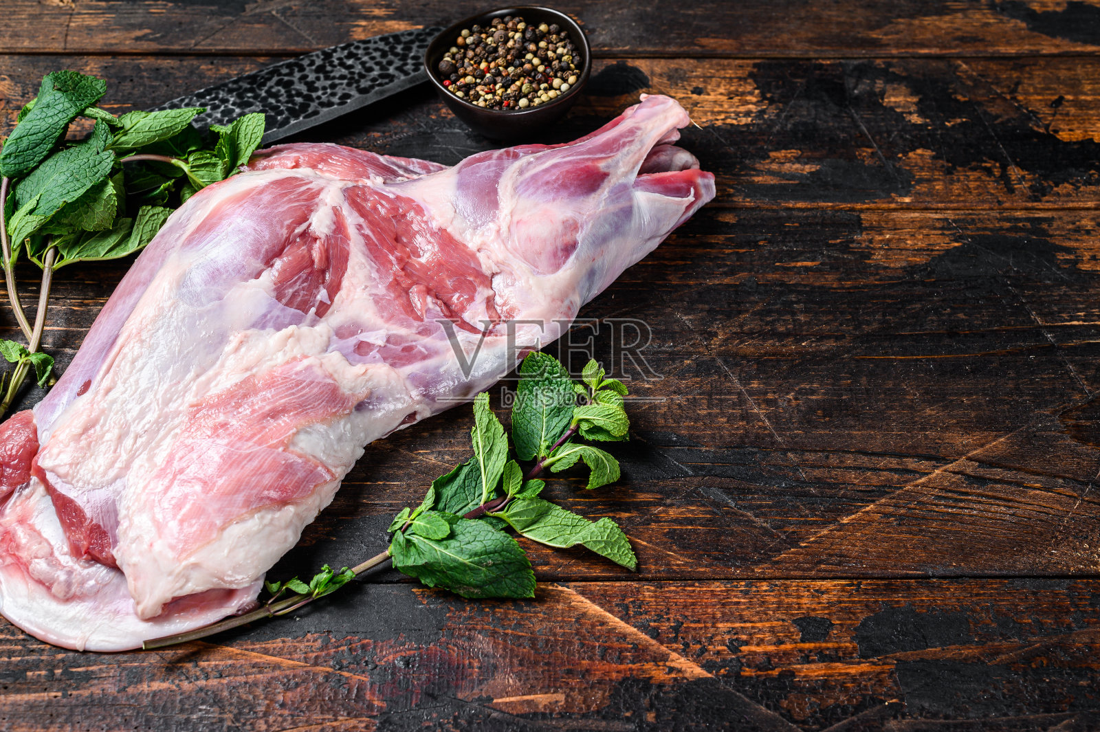 整只生羊肩腿肉加大蒜、薄荷。深色木制背景。前视图。本空间照片摄影图片