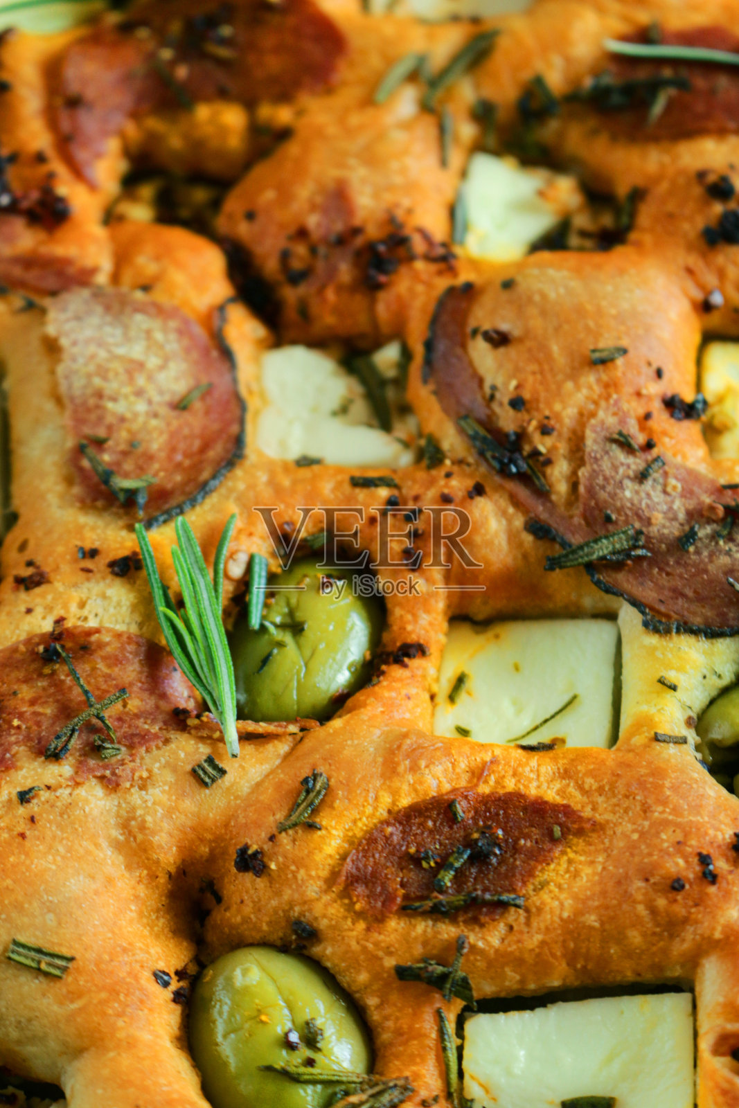 新鲜出炉的，自制的意大利佛卡夏面包，上面有绿橄榄，意大利腊肠和意大利辣香肠片，菲达奶酪和迷迭香叶装饰，高架视野照片摄影图片