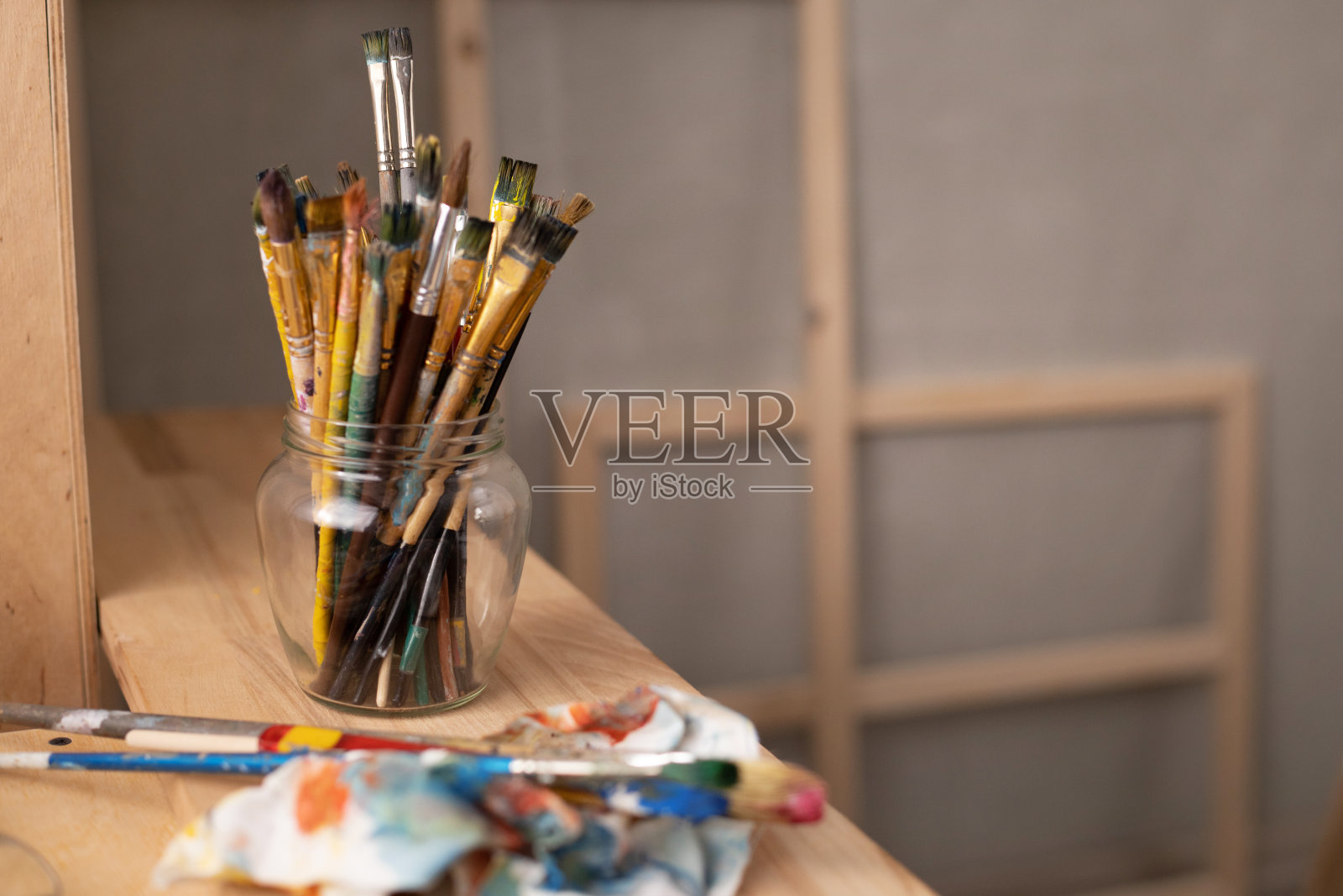 在木桌或窗台的玻璃罐中放置调色板和画笔。画笔和静物艺术照片摄影图片