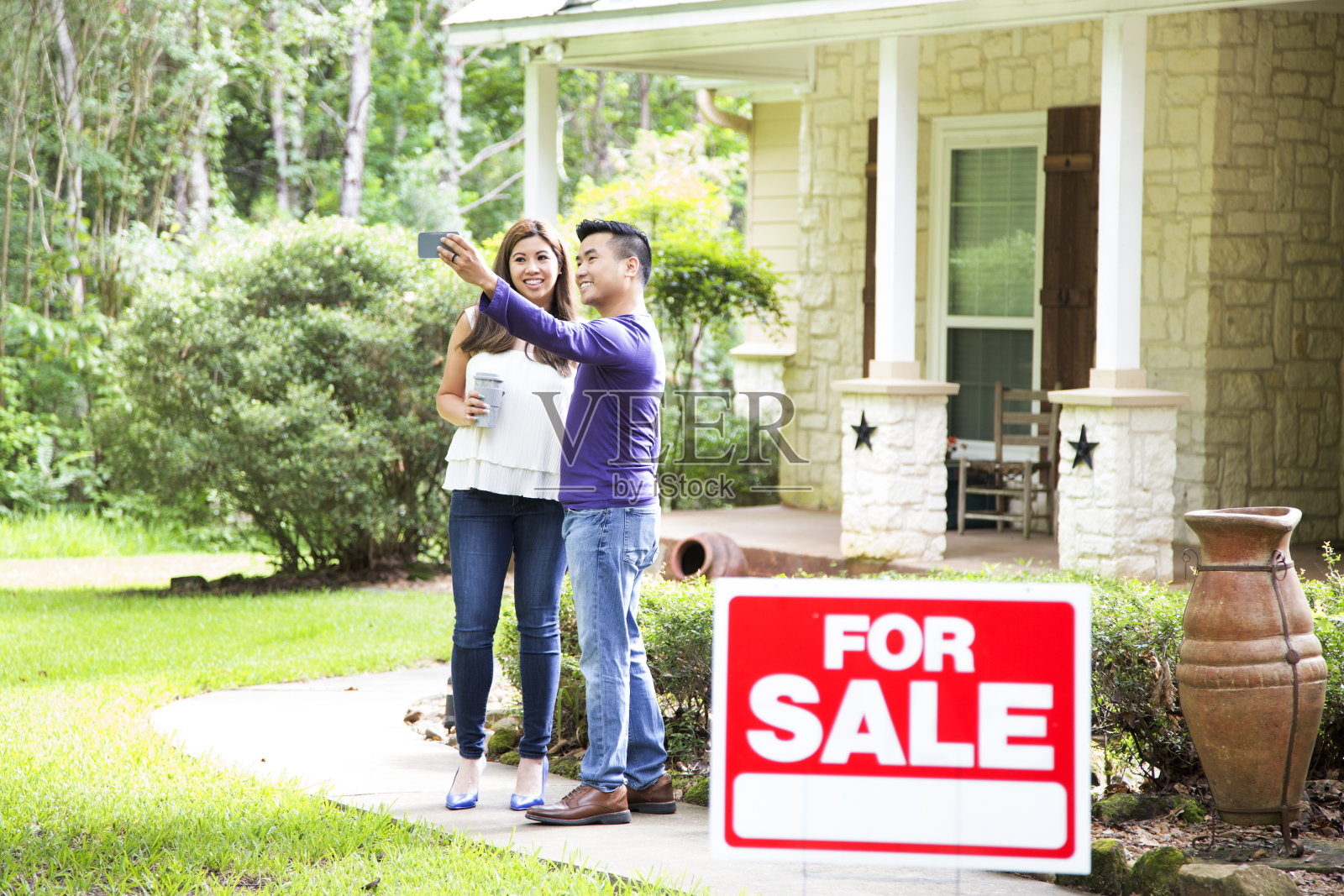 中年夫妇正在考虑购买一套新房子。出售的标志在前景。照片摄影图片