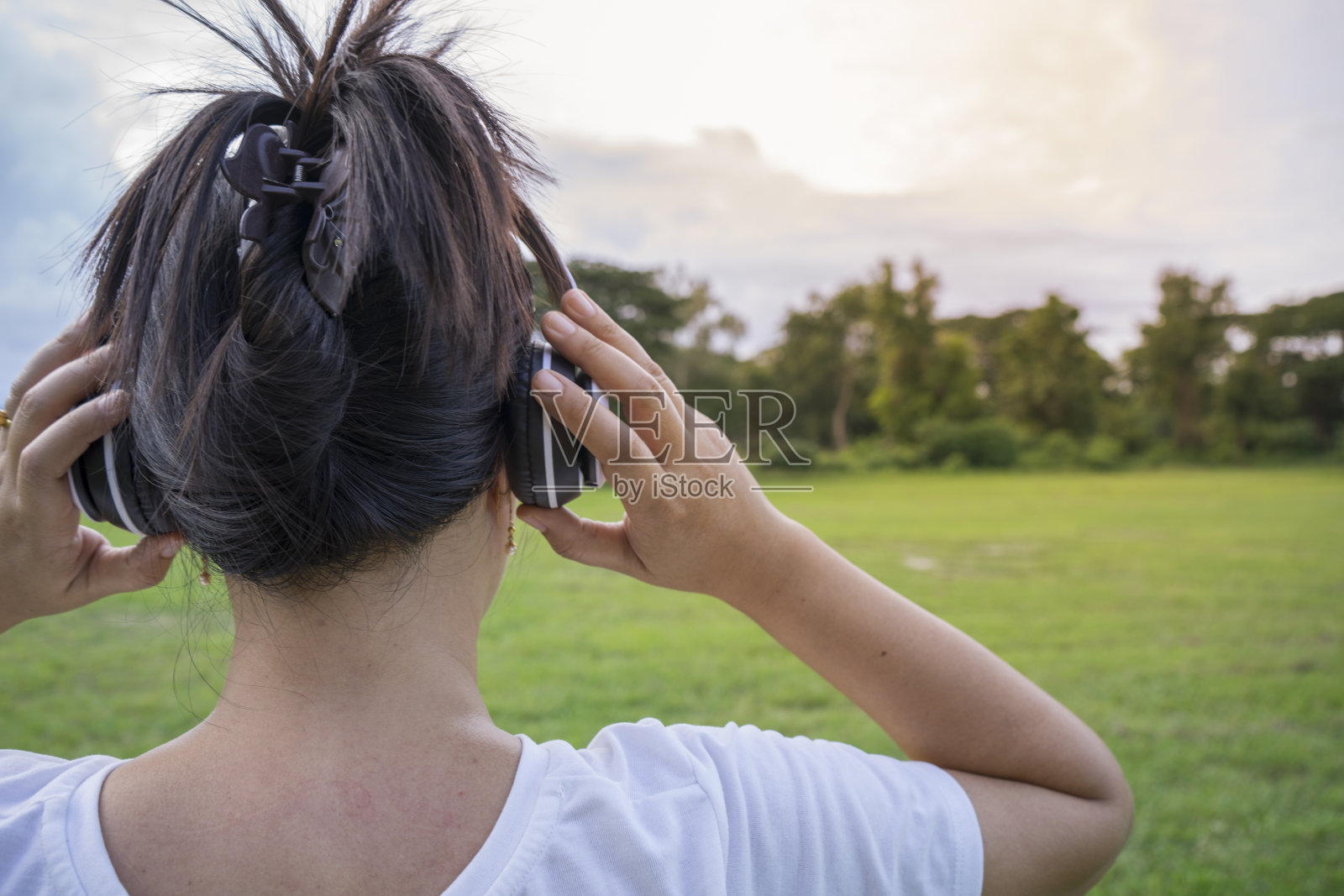 可爱的亚洲女人听音乐，手持白色耳机，背面拍摄。照片摄影图片