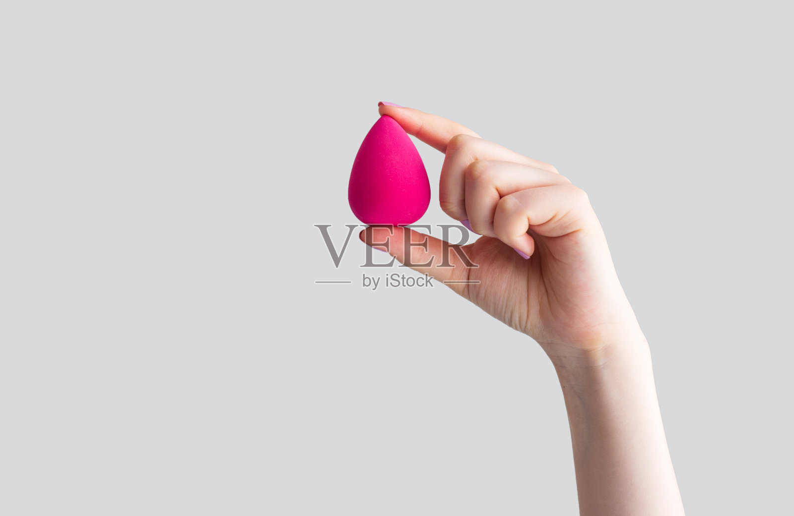 手握粉红色的蛋美丽海绵孤立在灰色的背景照片摄影图片