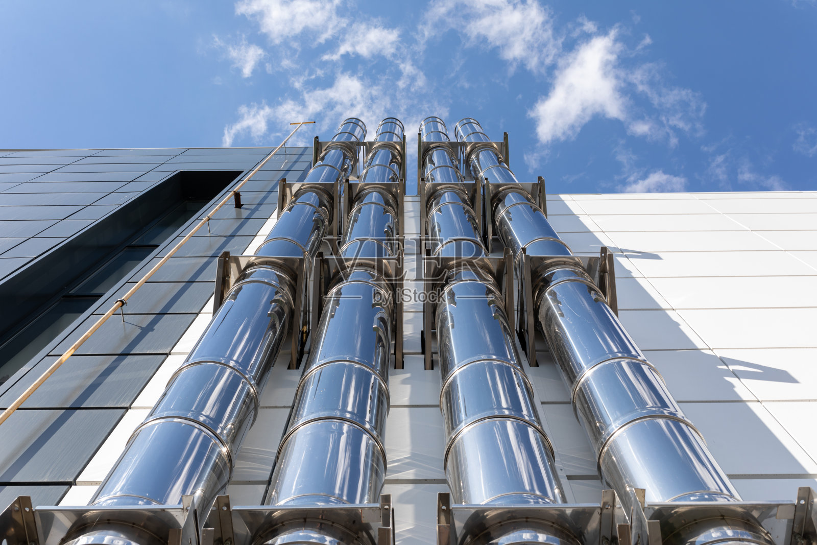 蓝色背景下的黑白工业建筑外墙的铬合金通风管道。自底向上的视图。照片摄影图片