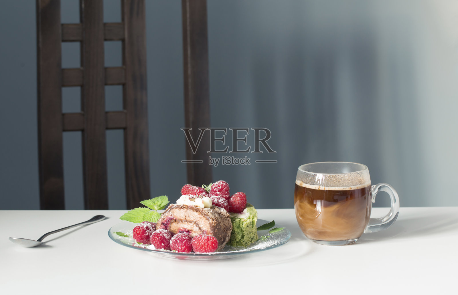 白色的桌子上放着一杯咖啡和带有覆盆子的甜点，背景是蓝色的墙壁照片摄影图片