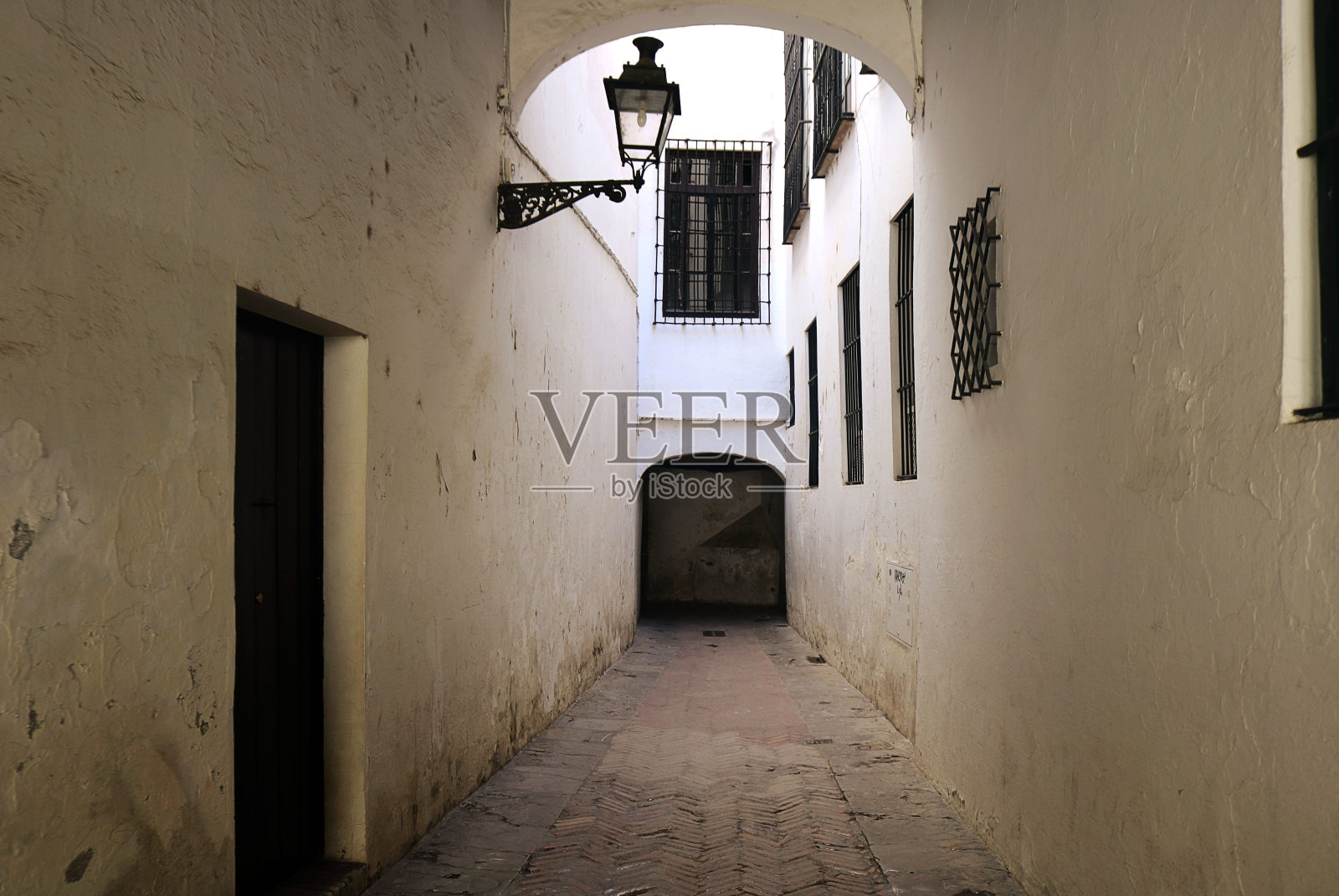 西班牙塞维利亚老城的传统狭窄街道——白色的墙，带栅栏的窗户，古老的门和一盏街灯照片摄影图片