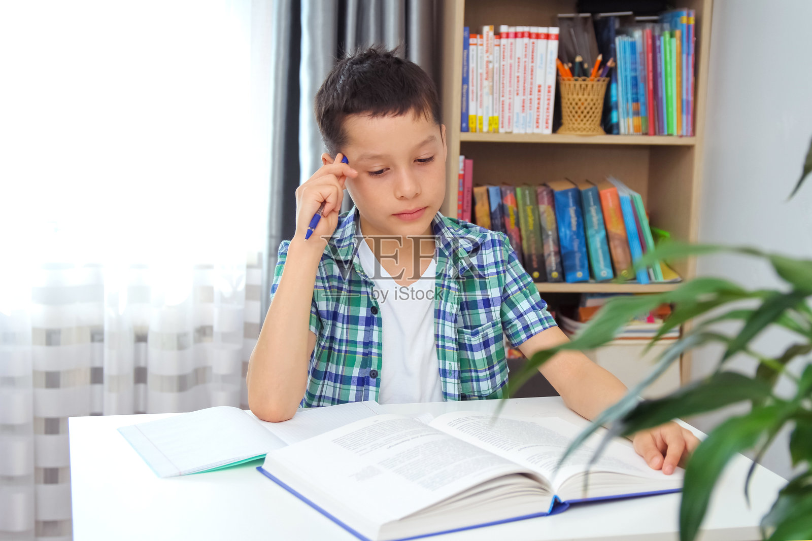 远程学习在线教育。一个男生在家里用笔记本电脑学习，做学校作业。训练书和笔记本放在桌上照片摄影图片