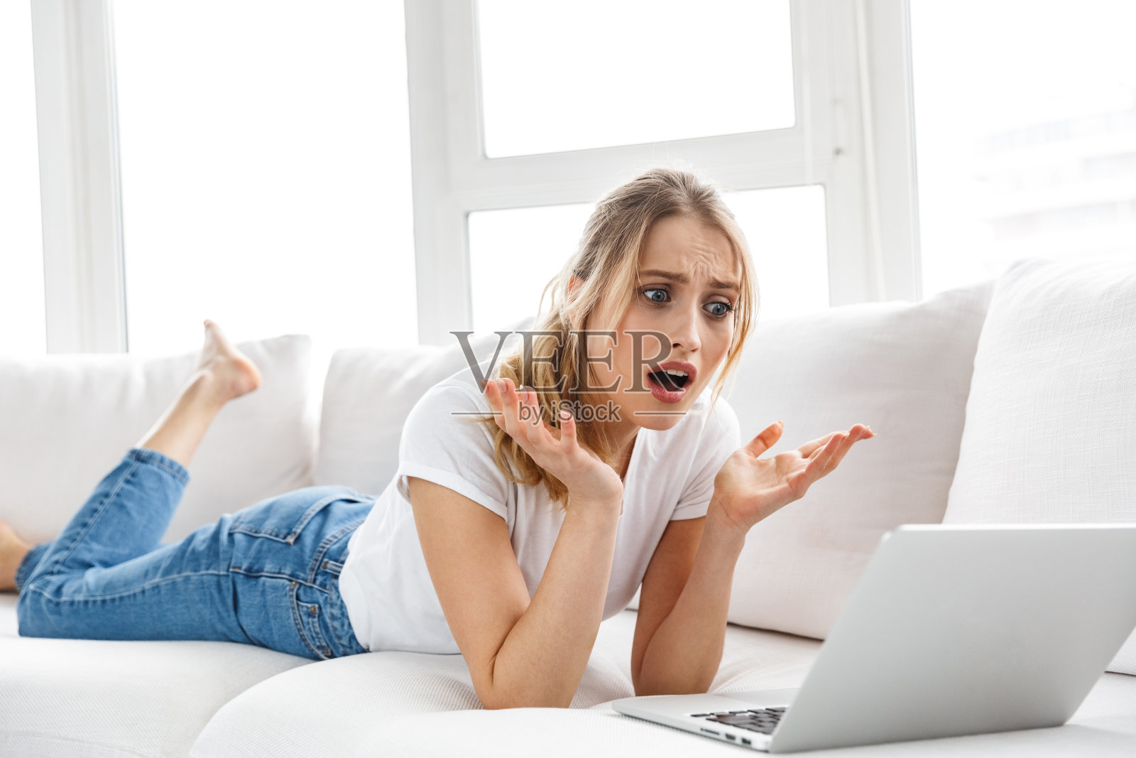 愤怒的20岁女孩躺在家里明亮的房间的沙发上使用笔记本电脑照片摄影图片