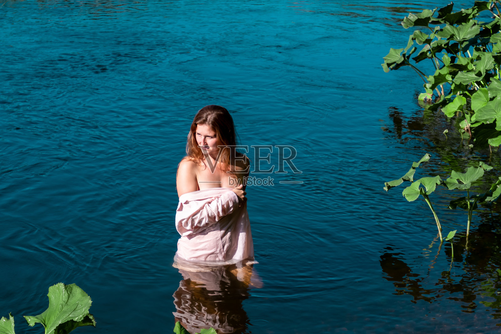 一名年轻女子在河里洗澡时穿着普通的衬衫，而不是泳衣照片摄影图片