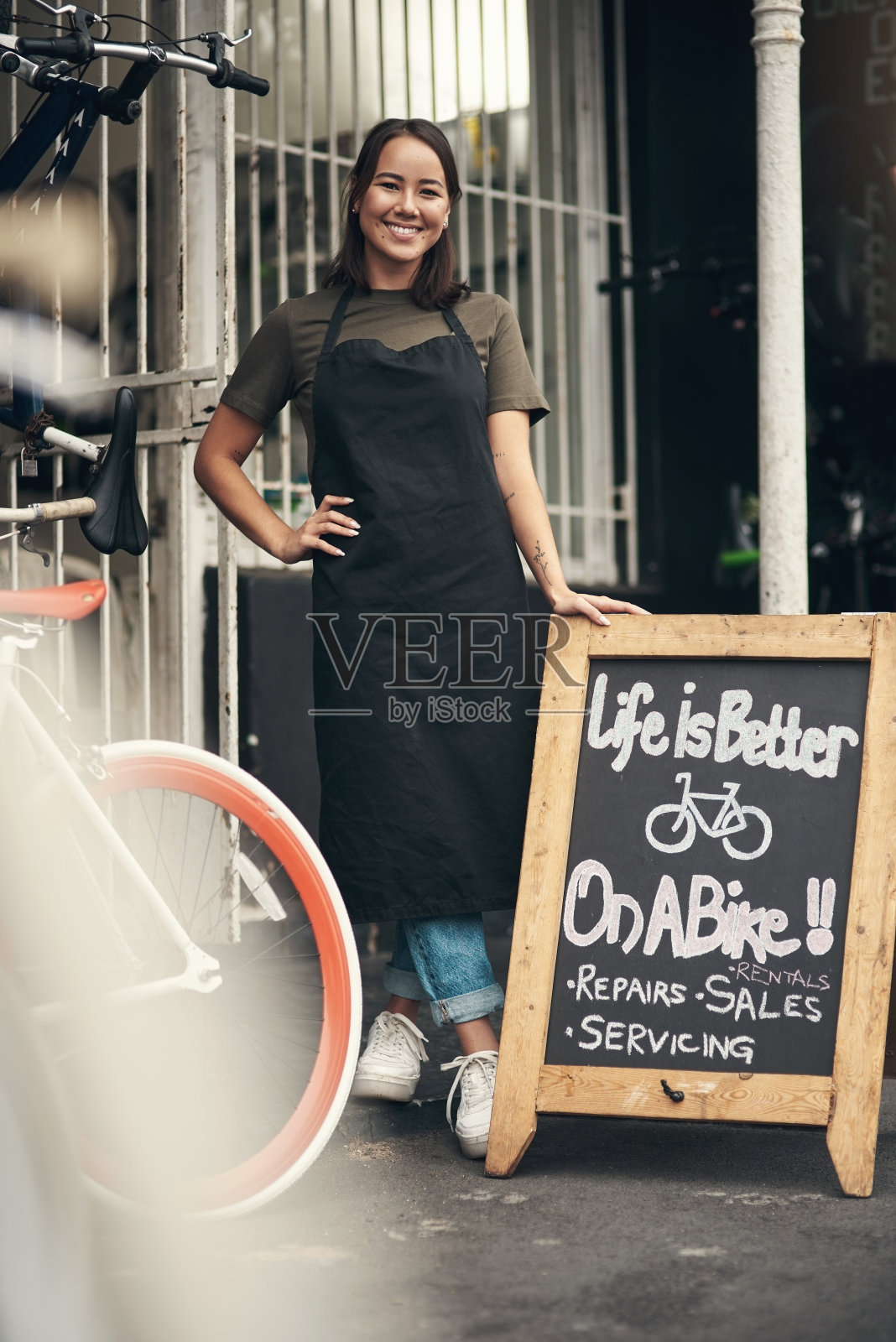 一个漂亮的年轻女人站在她的自行车店外面的全长照片在白天照片摄影图片